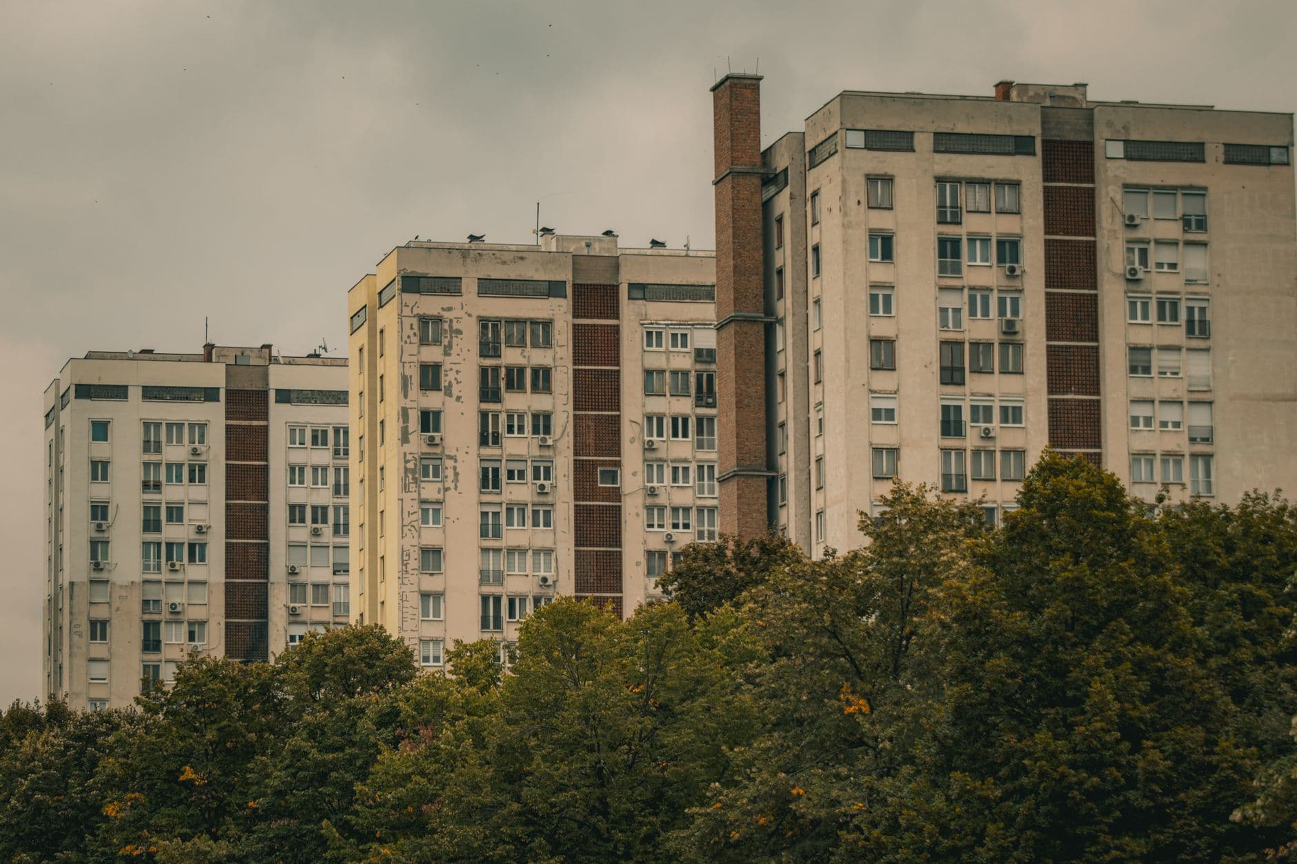 Series of urban apartment buildings on an overcast day, framed by trees.