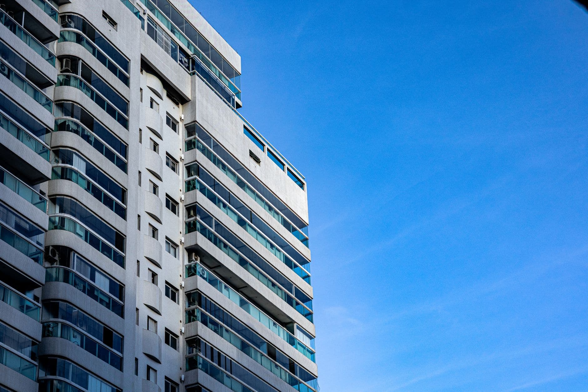 A modern high-rise building with glass balconies under a clear blue sky.