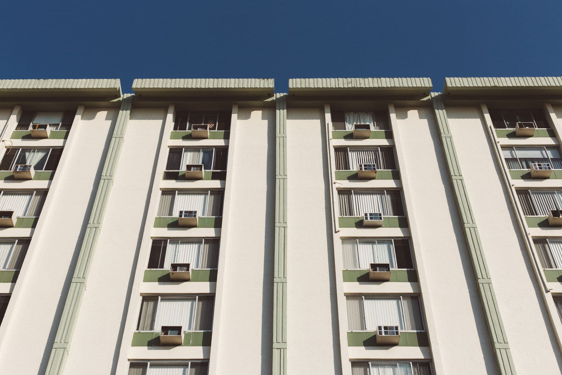 Low angle view of a residential building facade with air conditioning units and windows.