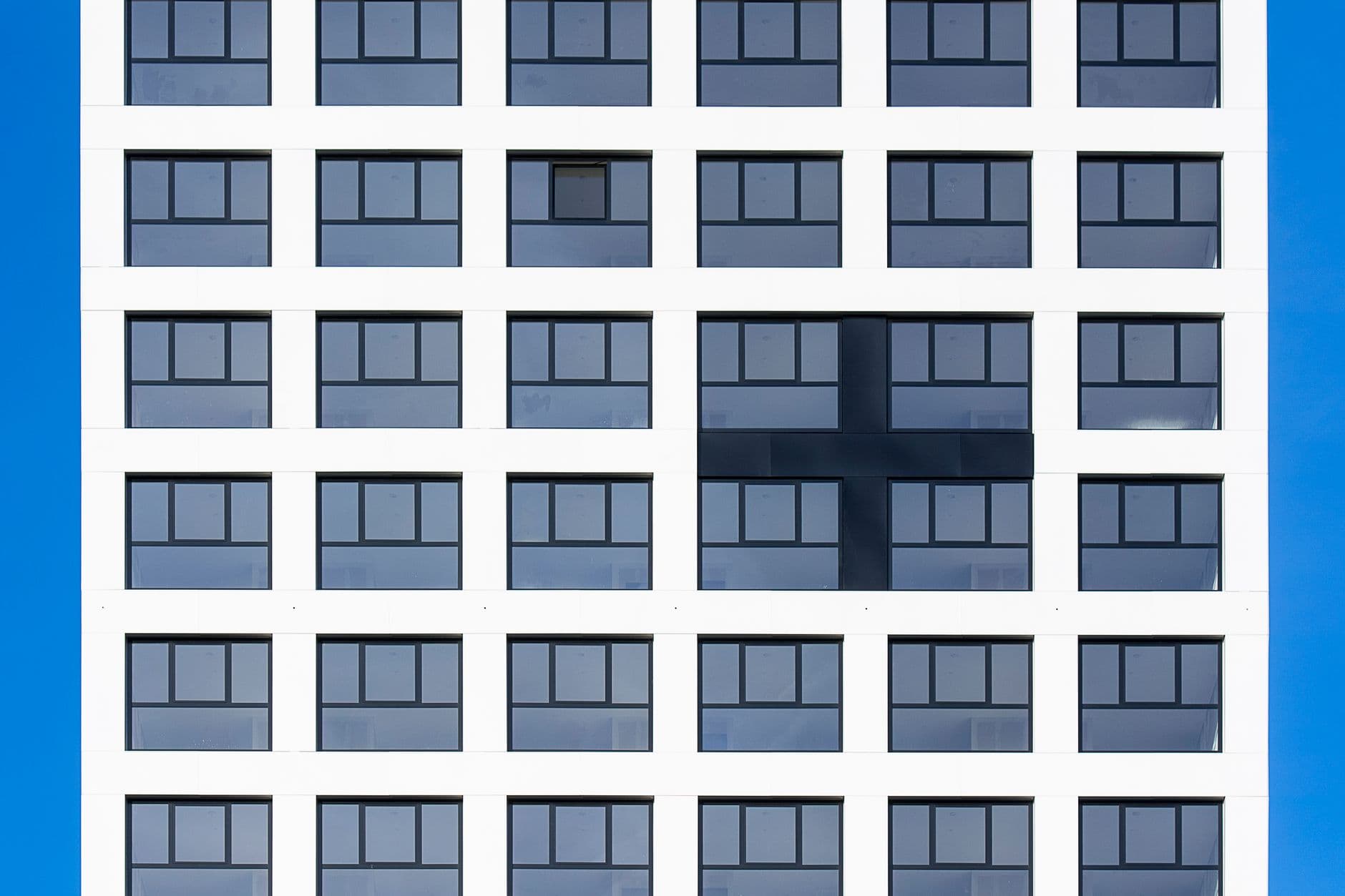Symmetrical building facade with unique cross pattern, blue sky backdrop.