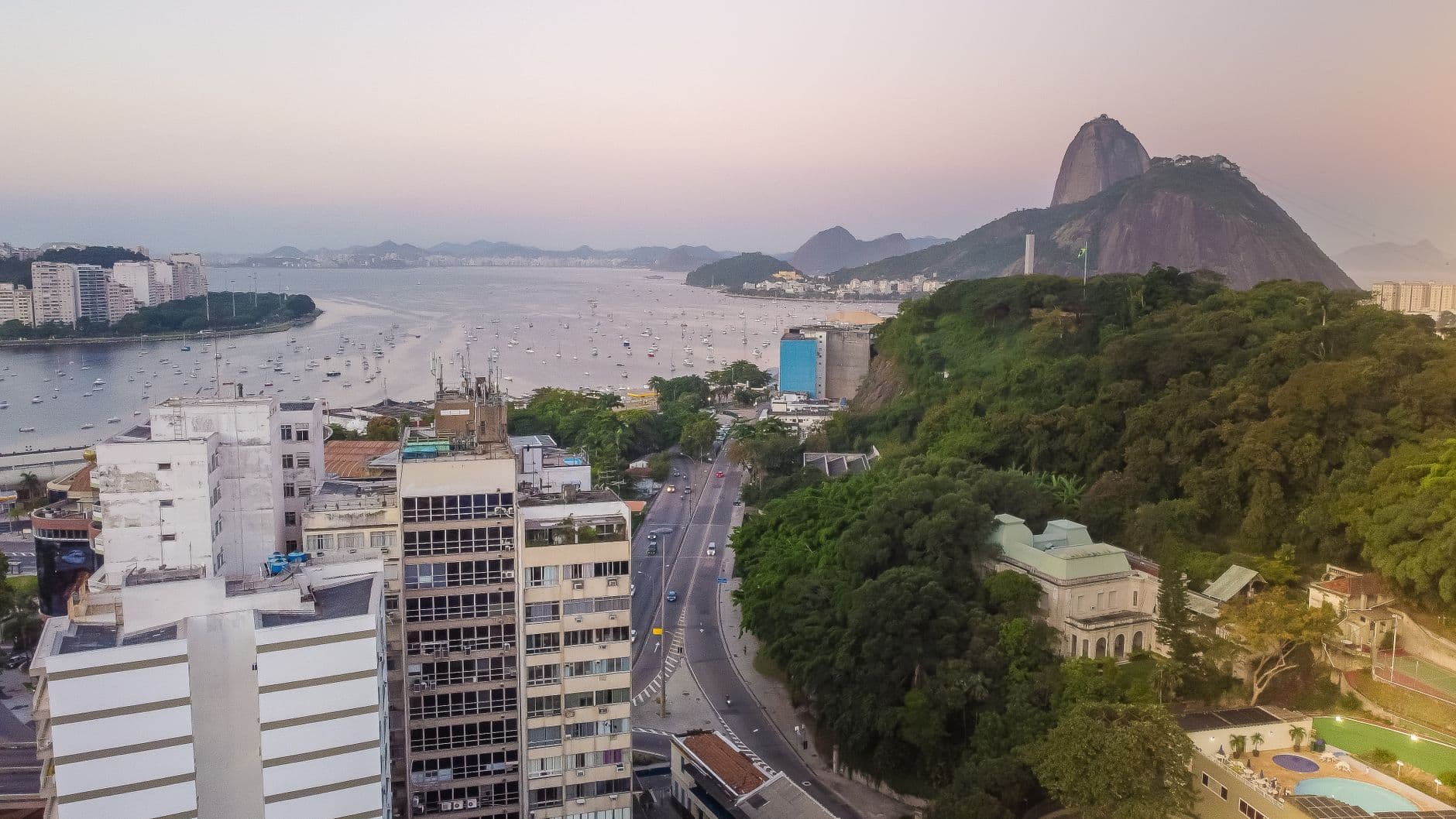 Stunning aerial view of Rio de Janeiro's coastline, highlighting the iconic Sugarloaf Mountain and urban landscape at sunset.