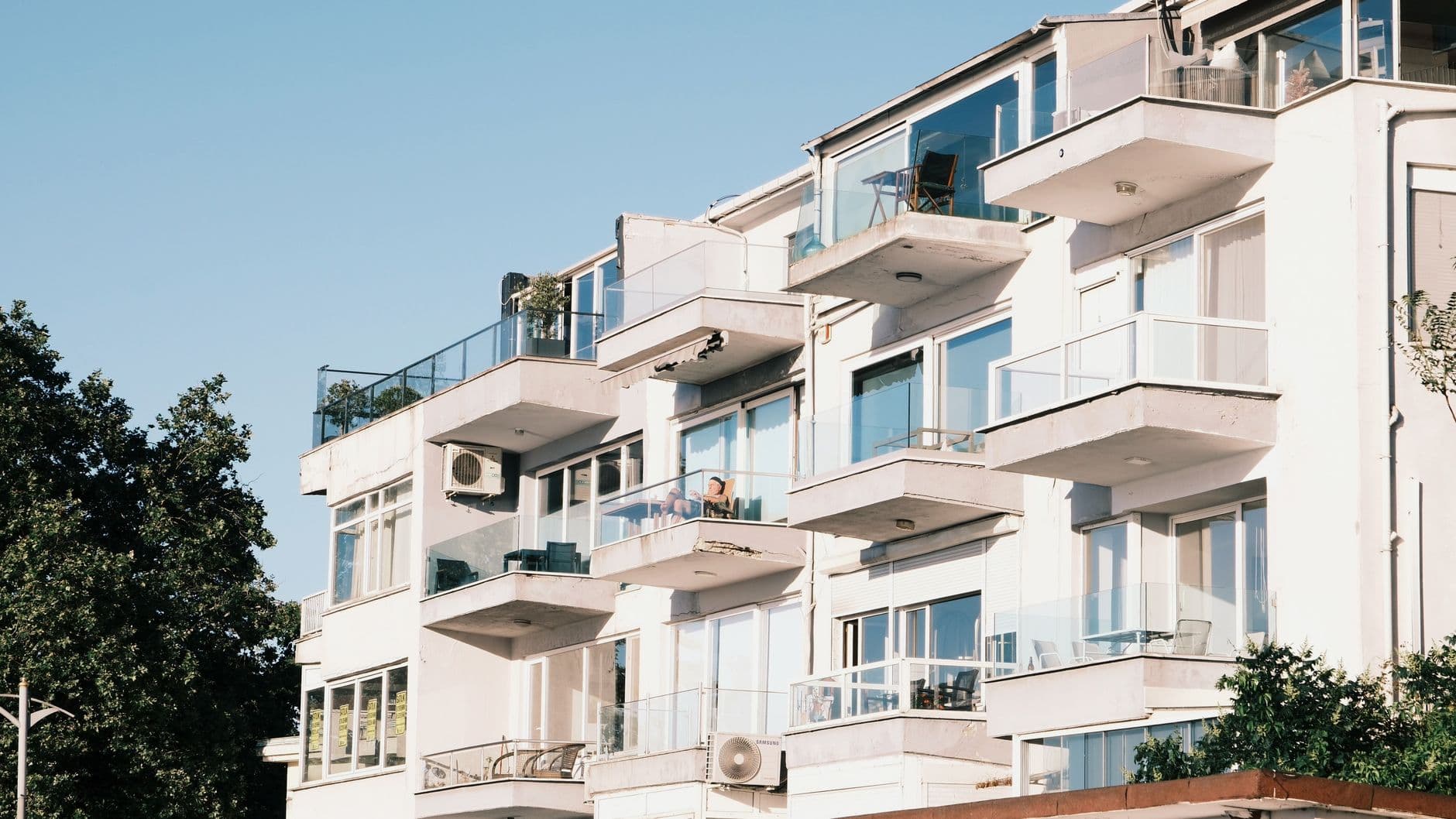 Contemporary apartment building showcasing glass balconies and summer ambiance.