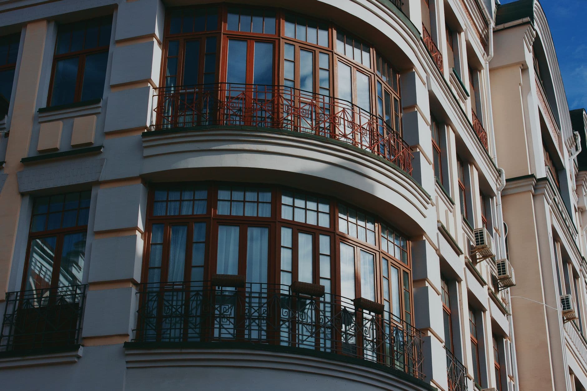 A stylish city building featuring curved balconies and large wooden-framed windows.