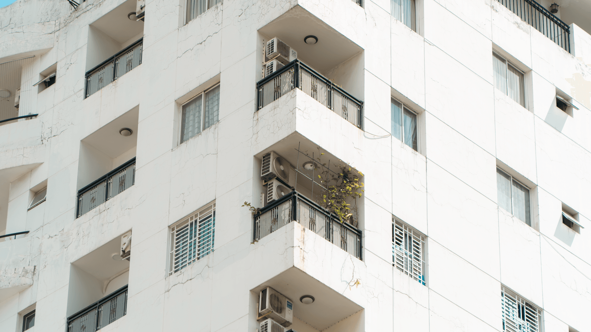 Exterior view of a white apartment building with balconies and air conditioning units.