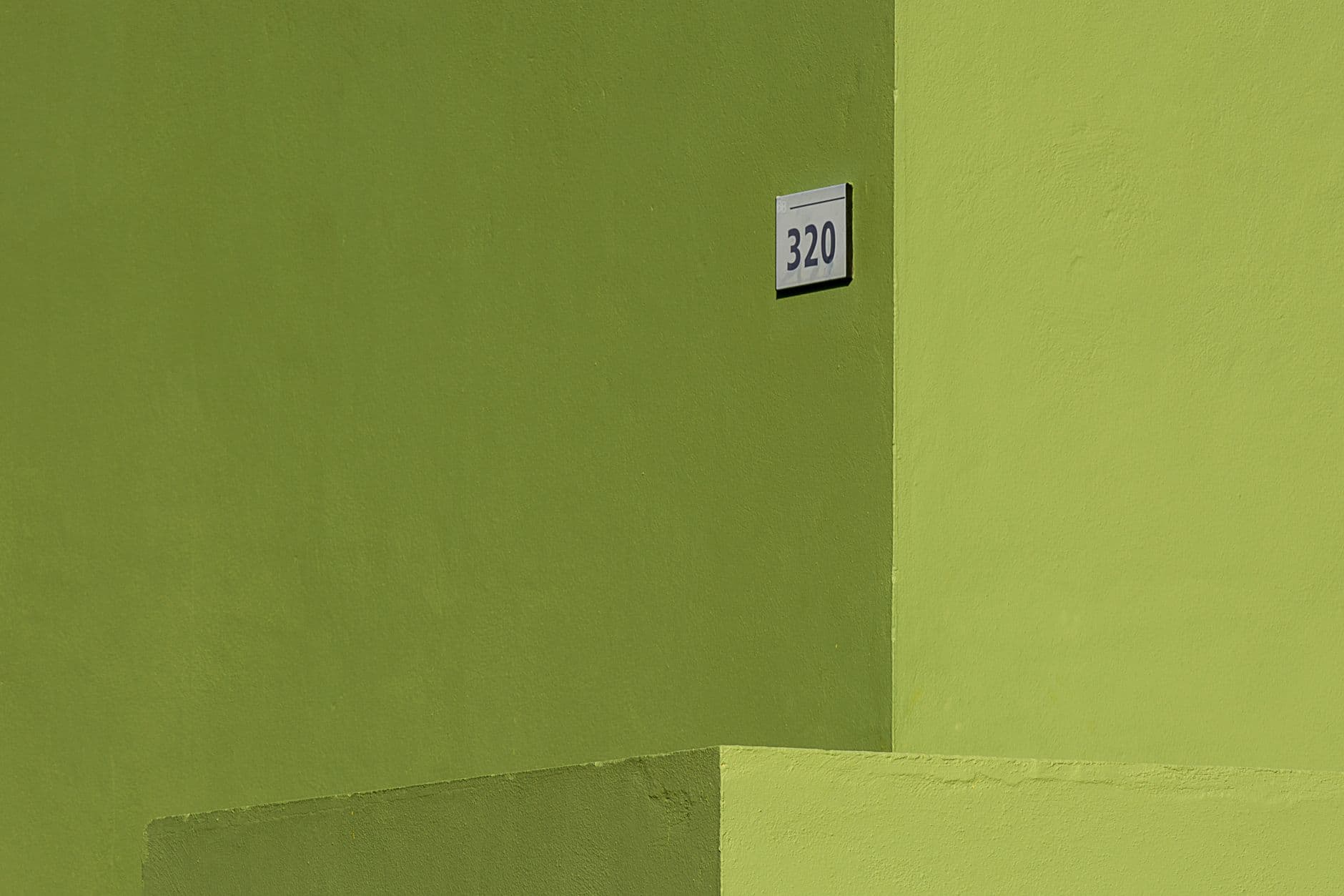 A minimalistic view of a bright green building facade featuring the number 320.