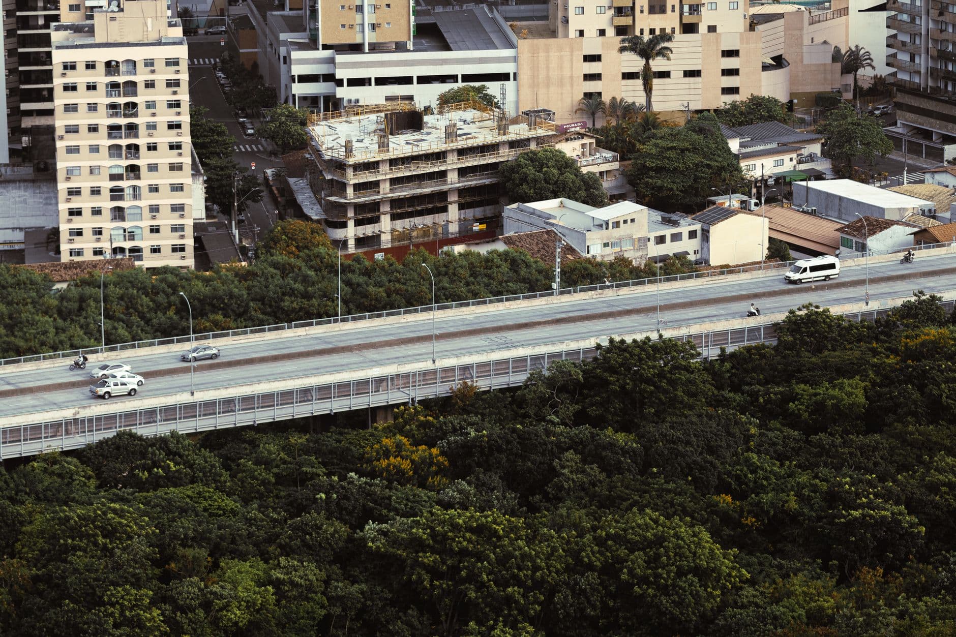 Aerial view of an urban highway surrounded by lush greenery and residential buildings in Brazil.