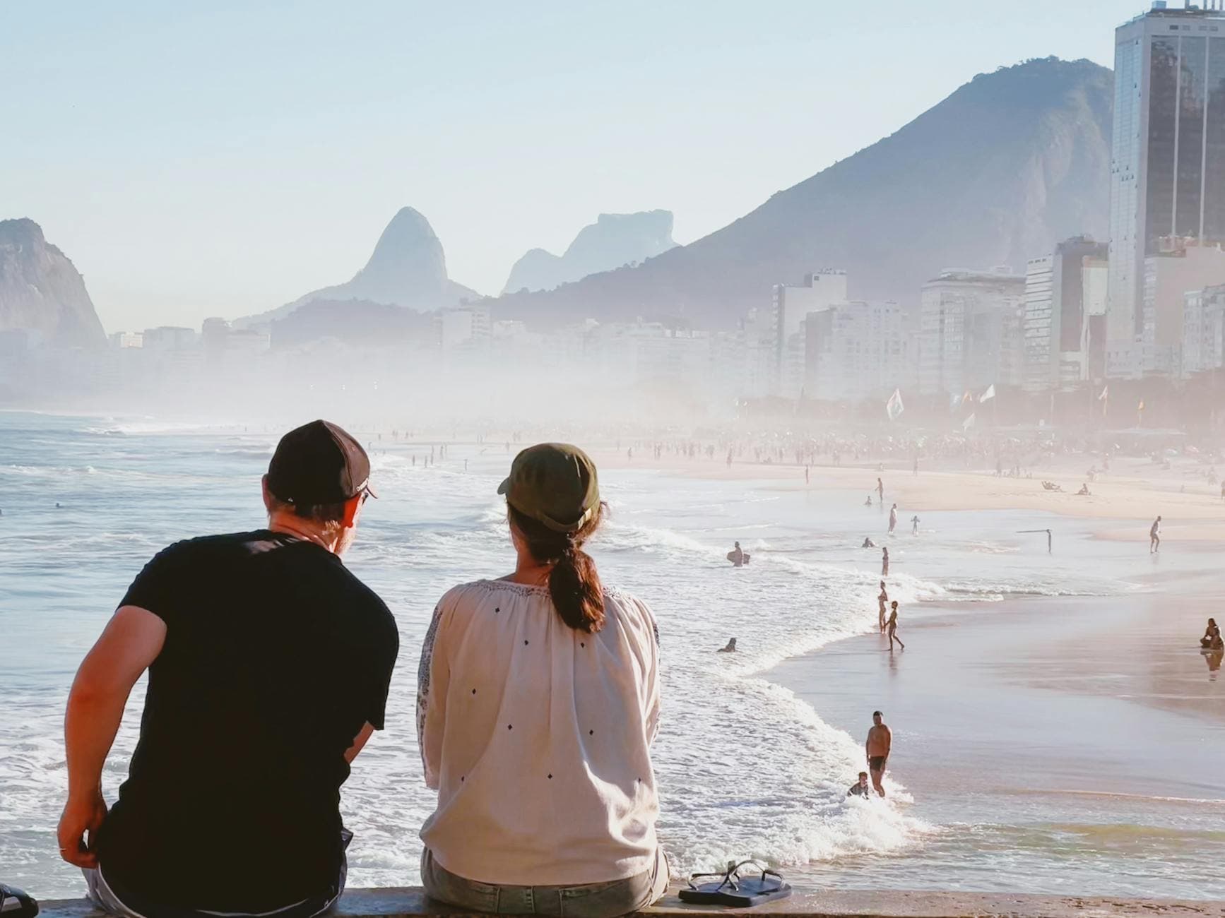 A couple sitting on a Rio de Janeiro beach admiring the sea and skyline.