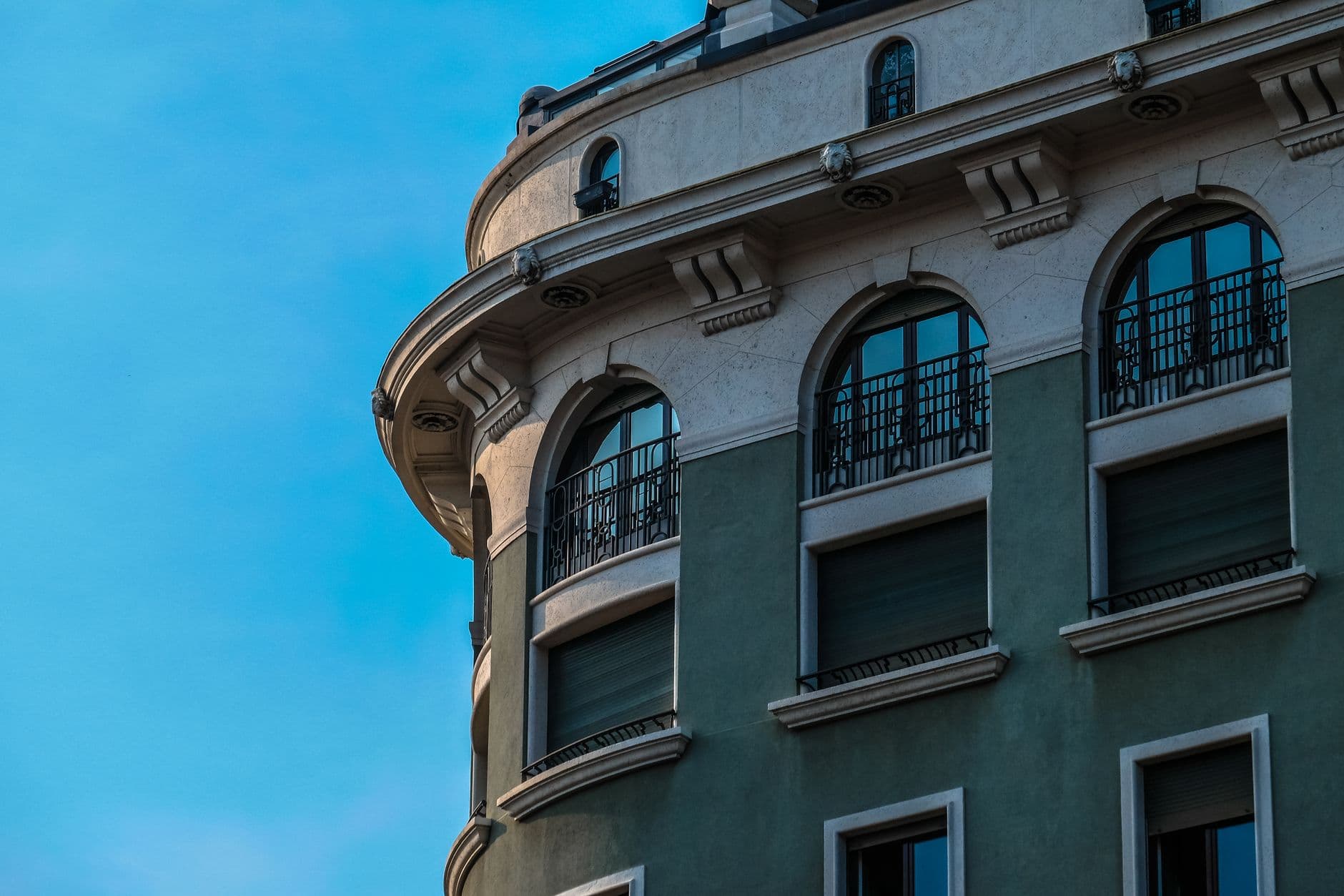 A green modern building with ornate arched windows and balconies against a clear blue sky.