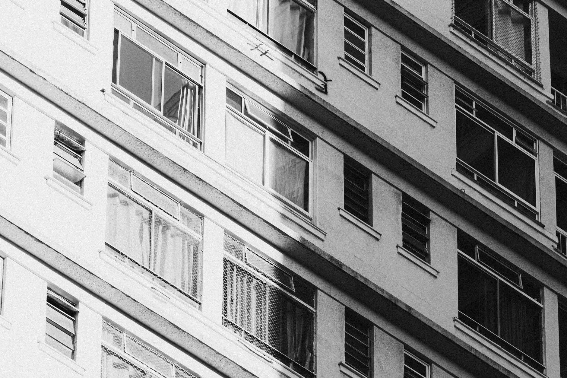 A low angle black and white photo of a building facade with geometrical window designs.