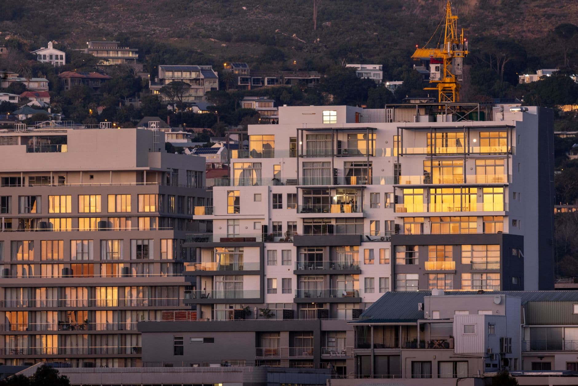Urban residential buildings reflecting sunset light with a crane in the backdrop.