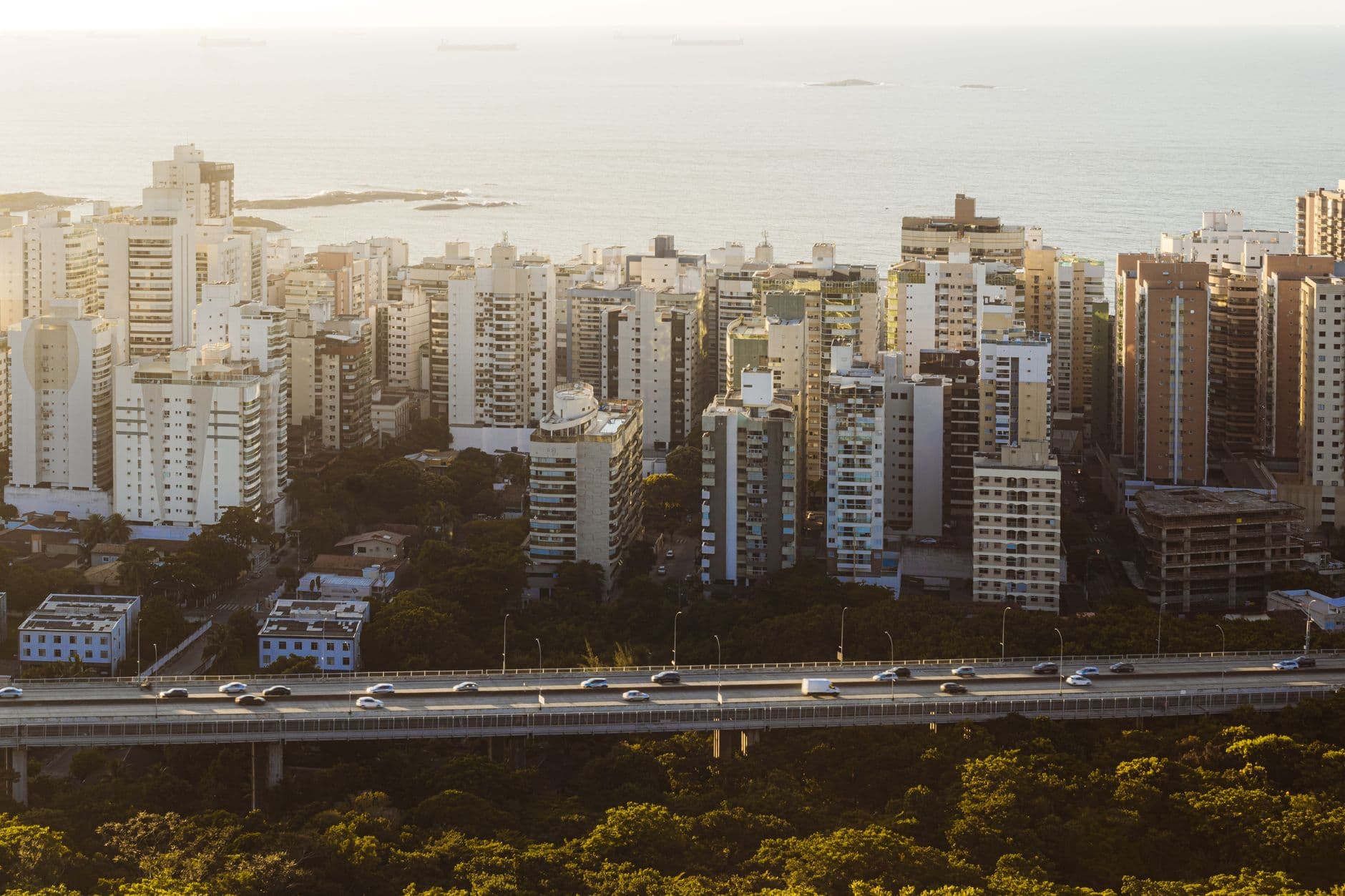 High-rise buildings overlooking the ocean with a highway, captured during sunset, in a coastal city.