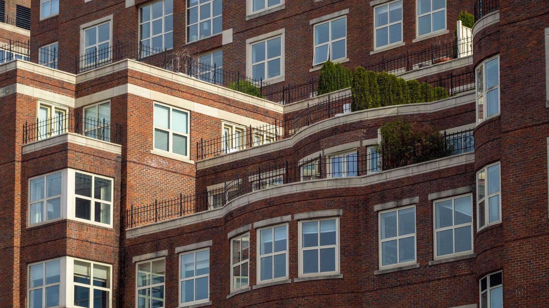 Detailed view of a red brick apartment building with terraces and greenery.