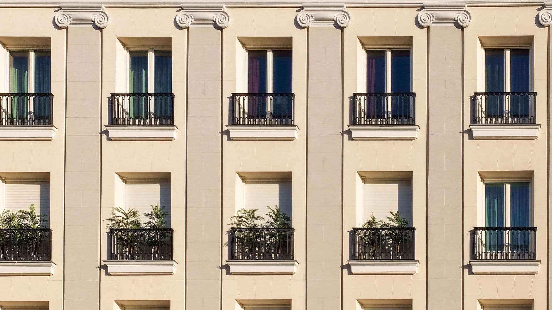 Elegant building exterior with classic windows and balconies adorned with plants.