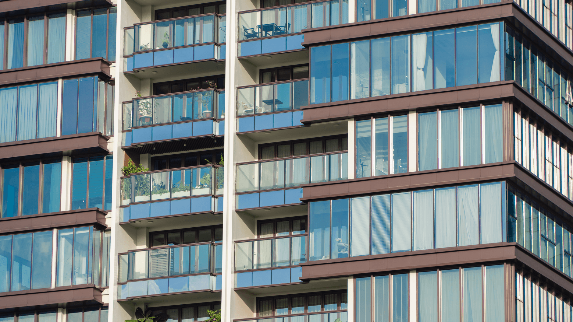 Close-up view of modern glass apartment facade with balconies and reflections.