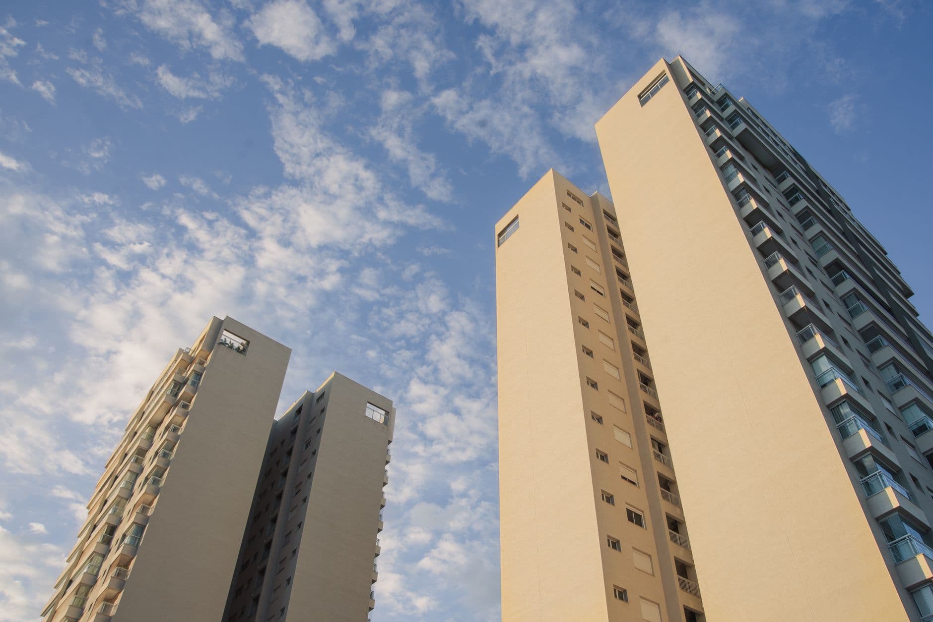 Low angle view of modern high-rise residential buildings under a bright blue sky with scattered clouds.