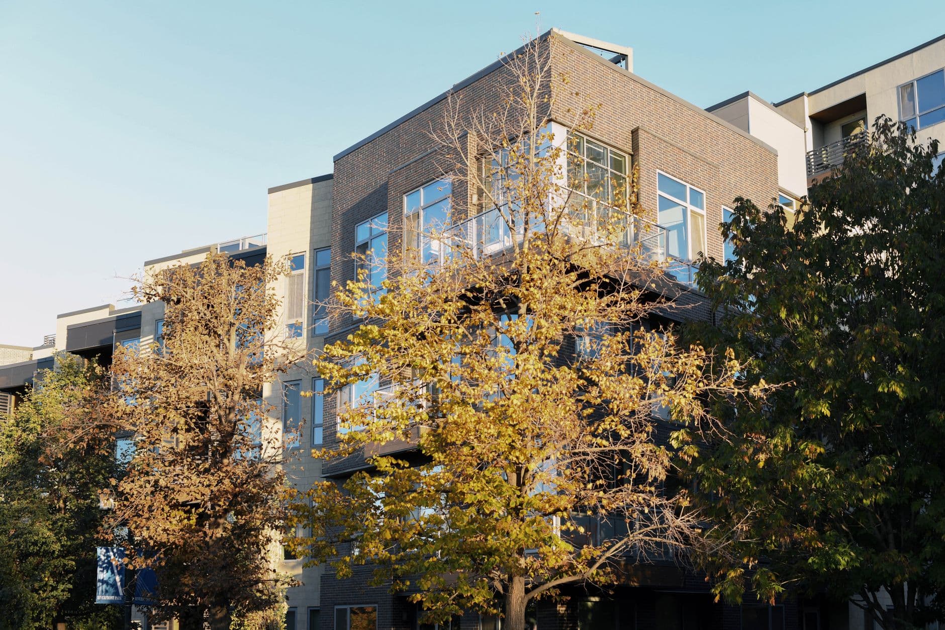 Modern apartment building surrounded by autumn trees under clear blue sky.