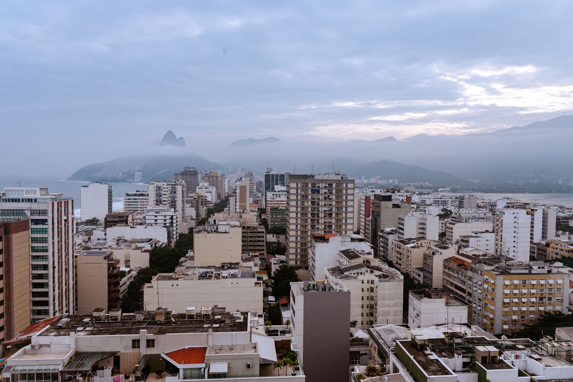 Aerial cityscape of Rio de Janeiro with misty mountains and coastal view during overcast weather.
