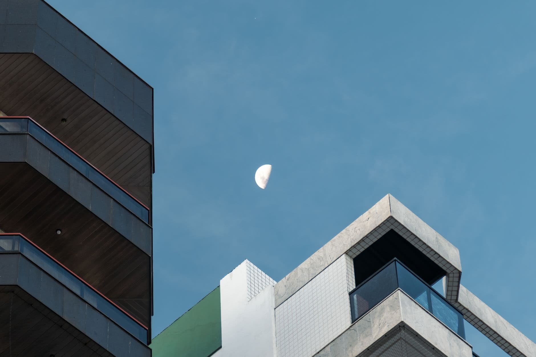 Modern apartment buildings with a visible moon against a clear blue sky.
