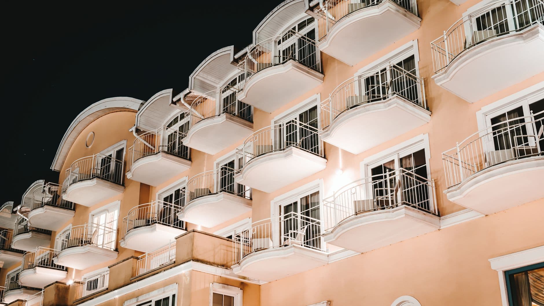 Low angle view of a modern building with balconies lit at night, showcasing architectural elegance.