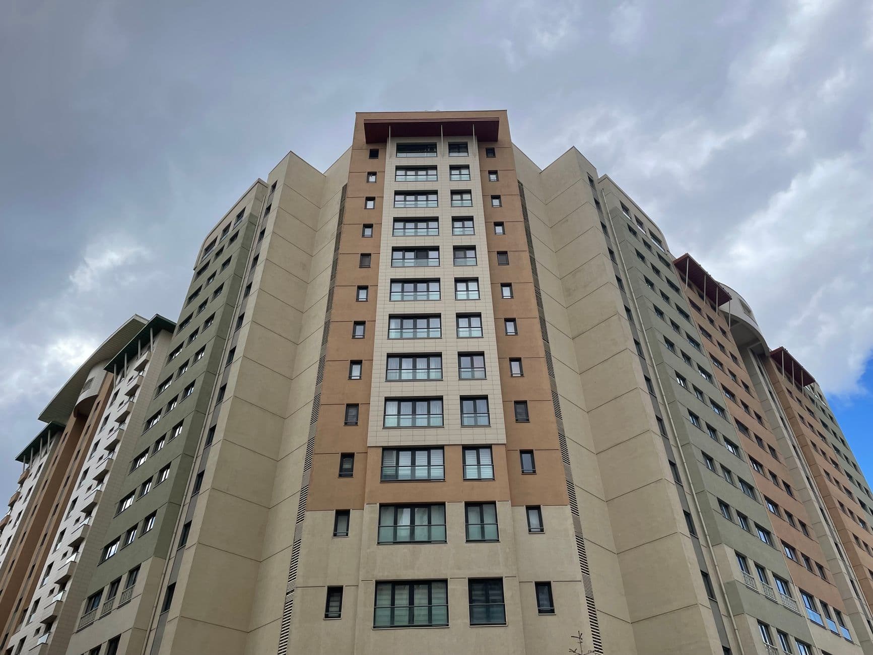 Low angle view of a modern residential skyscraper with geometric design and cloudy sky backdrop.