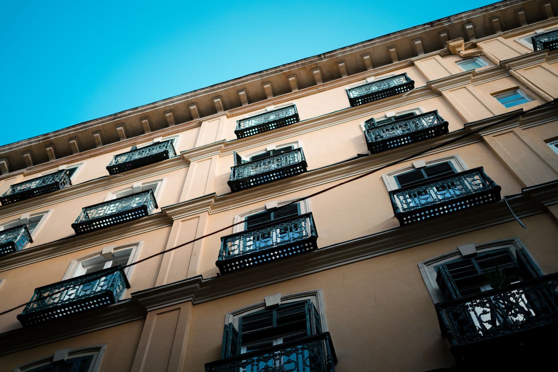 Upward view of a European building facade with ornate iron balconies under clear blue sky.